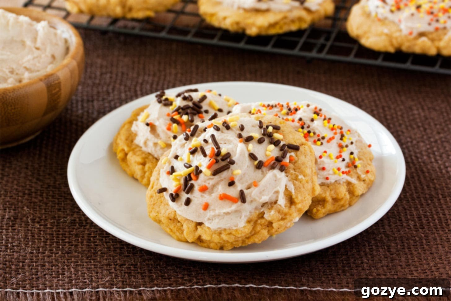 Pumpkin spice cookies topped with cinnamon frosting and sprinkles on a white plate