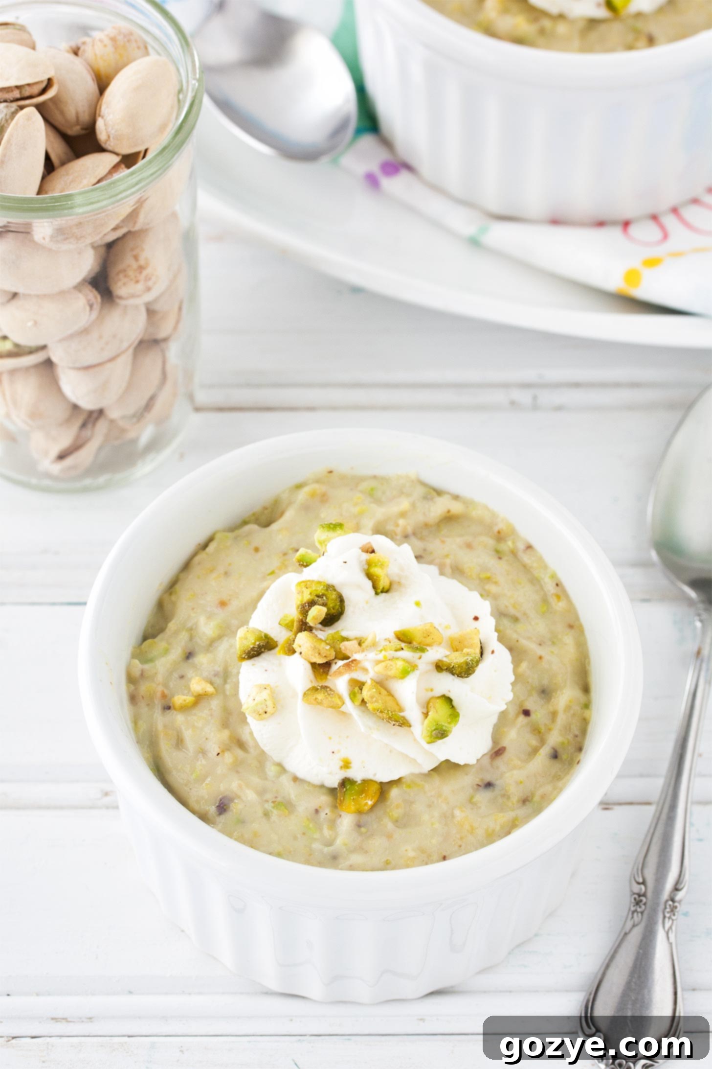 A vibrant green pistachio pudding cup, topped generously with fluffy homemade whipped cream and garnished with finely chopped pistachios, ready to be enjoyed.