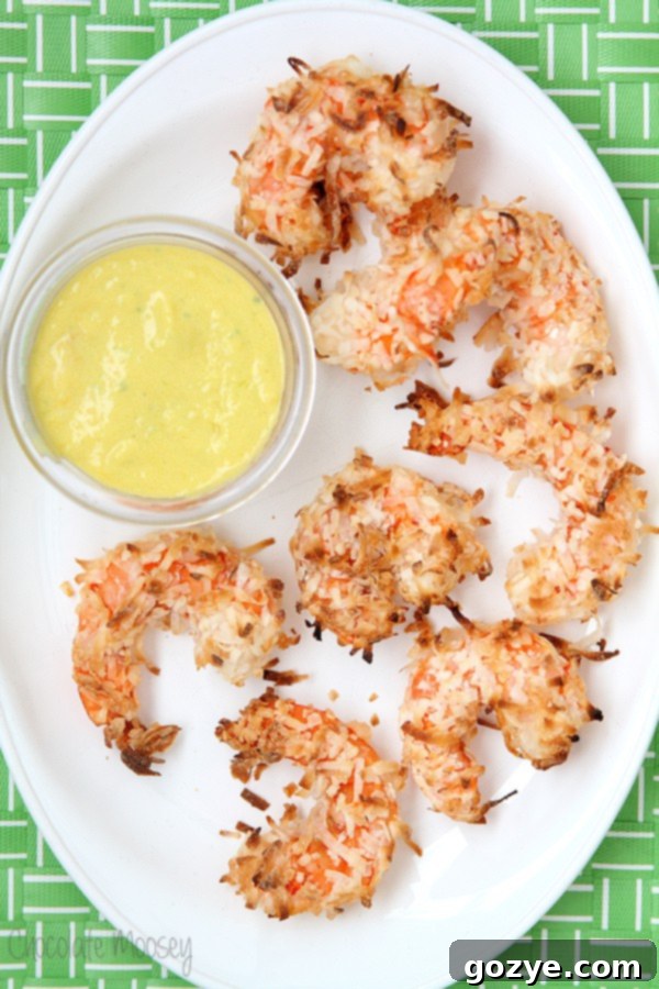 Healthy coconut shrimp glistening with a crispy coating, arranged artfully with a small bowl of mango dipping sauce