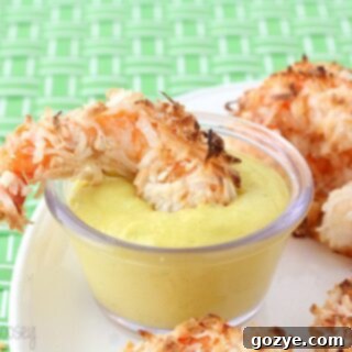 Baked Coconut Shrimp being dipped into a vibrant mango yogurt sauce