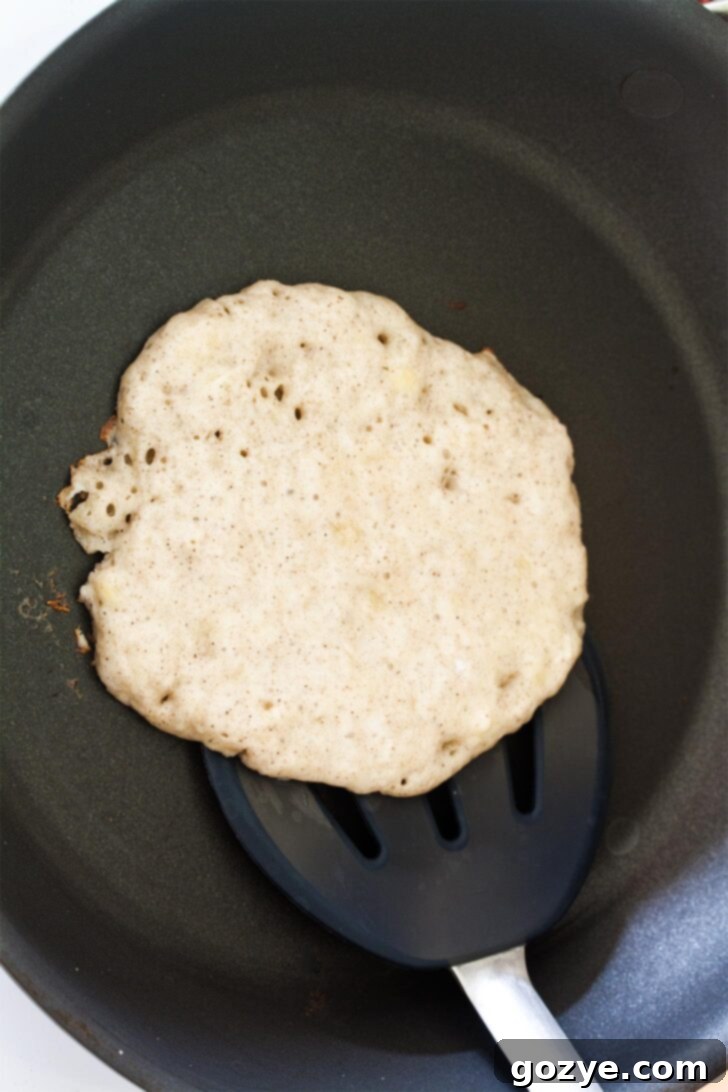 Dairy-Free Banana Coconut Milk Pancakes 6 A spatula flipping a dairy-free coconut milk pancake on a hot skillet, showing the golden-brown underside.