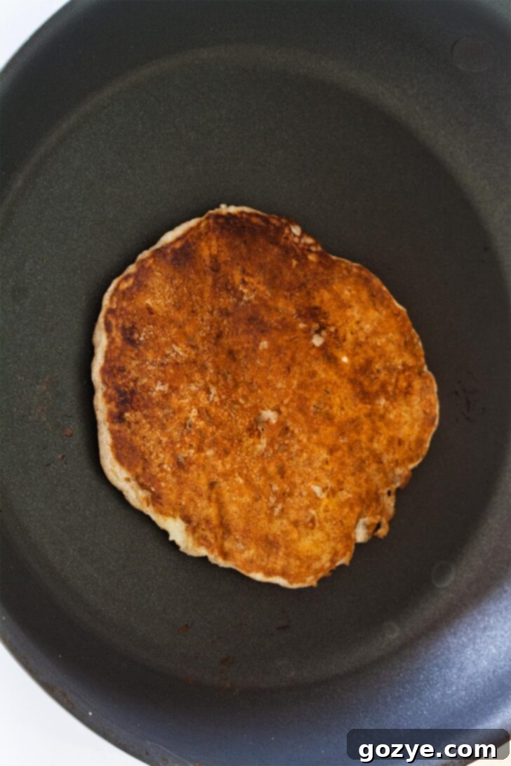 Dairy-Free Banana Coconut Milk Pancakes 7 Two golden-brown banana pancakes resting on a cooling rack, showcasing their fluffy texture and readiness for serving.