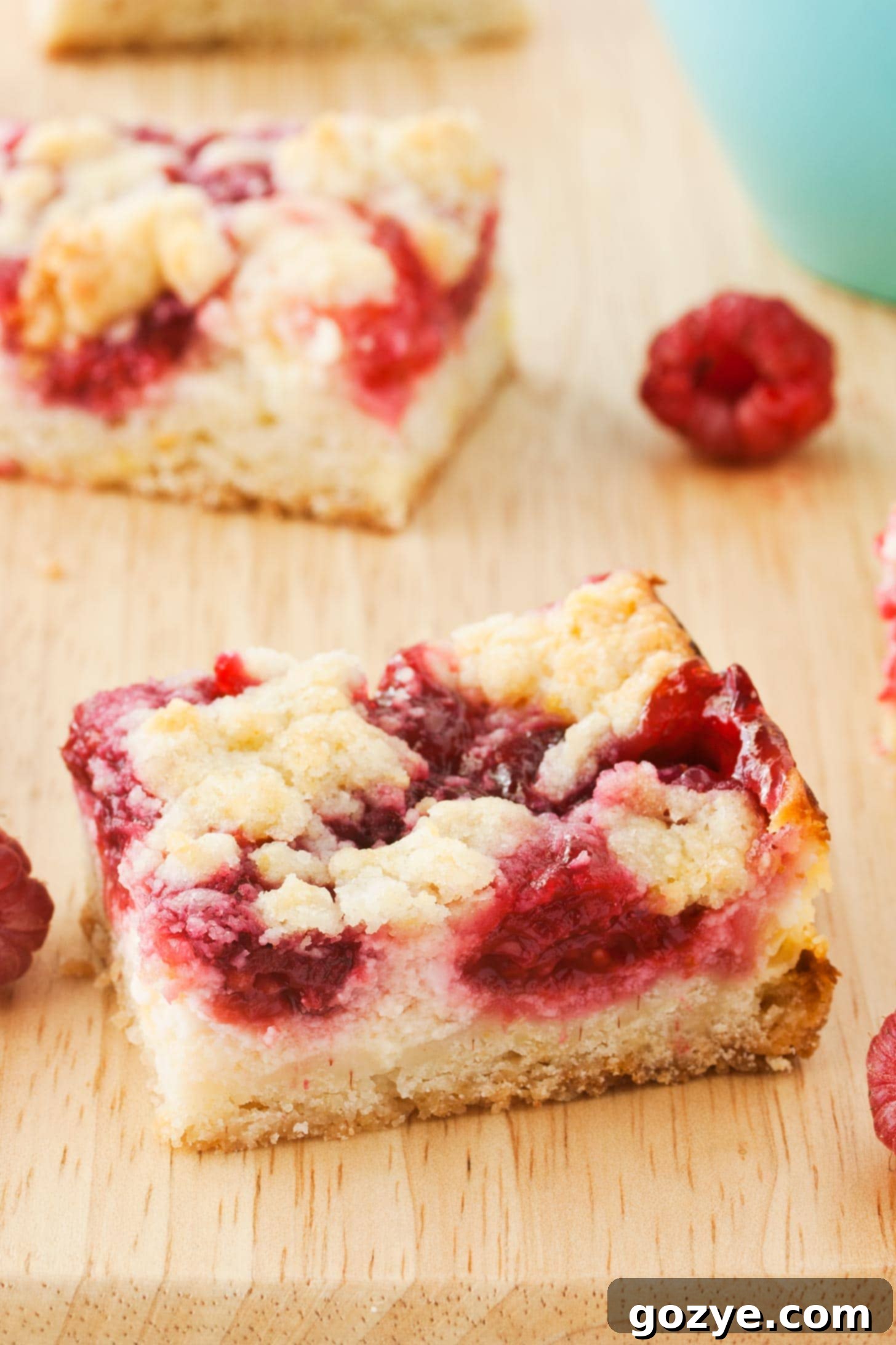 Raspberry Cheesecake Bars on a cutting board with berries