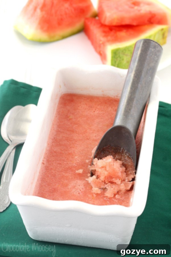 Scooping homemade Watermelon Italian Ice from a white freezer-safe pan, highlighting its icy texture.