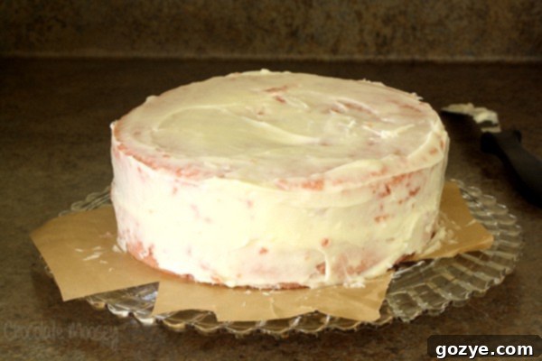 Applying a crumb coat of cream cheese frosting to a homemade strawberry layer cake