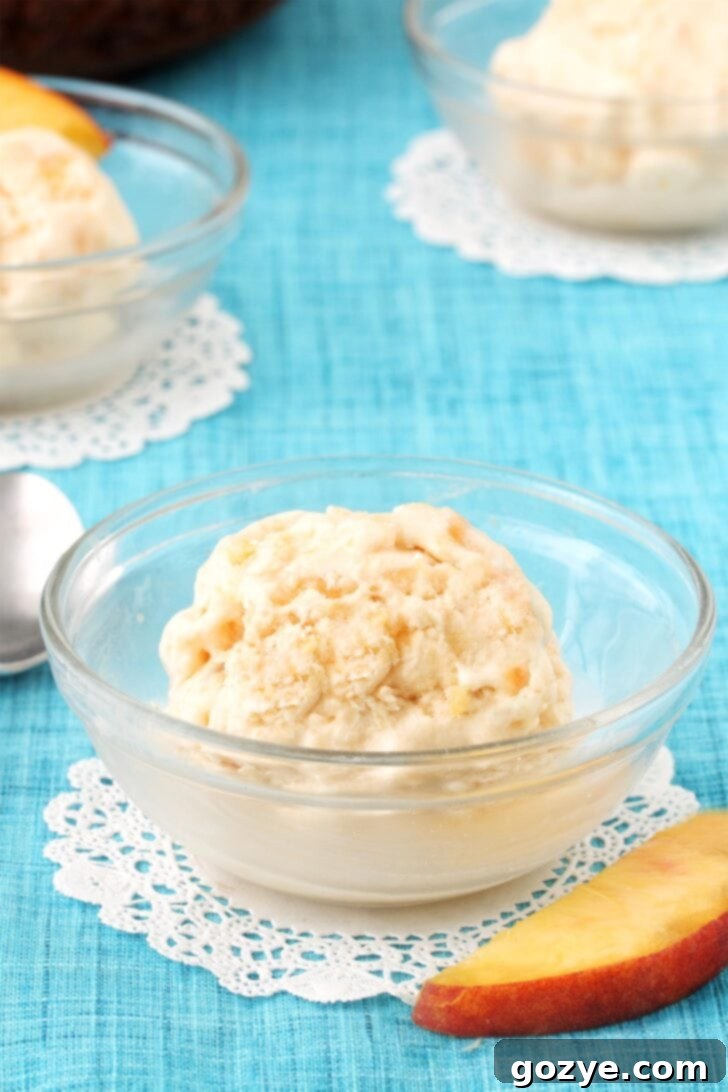 Two scoops of peach ice cream in a small glass bowl, garnished with a fresh mint leaf, on a rustic wooden surface.