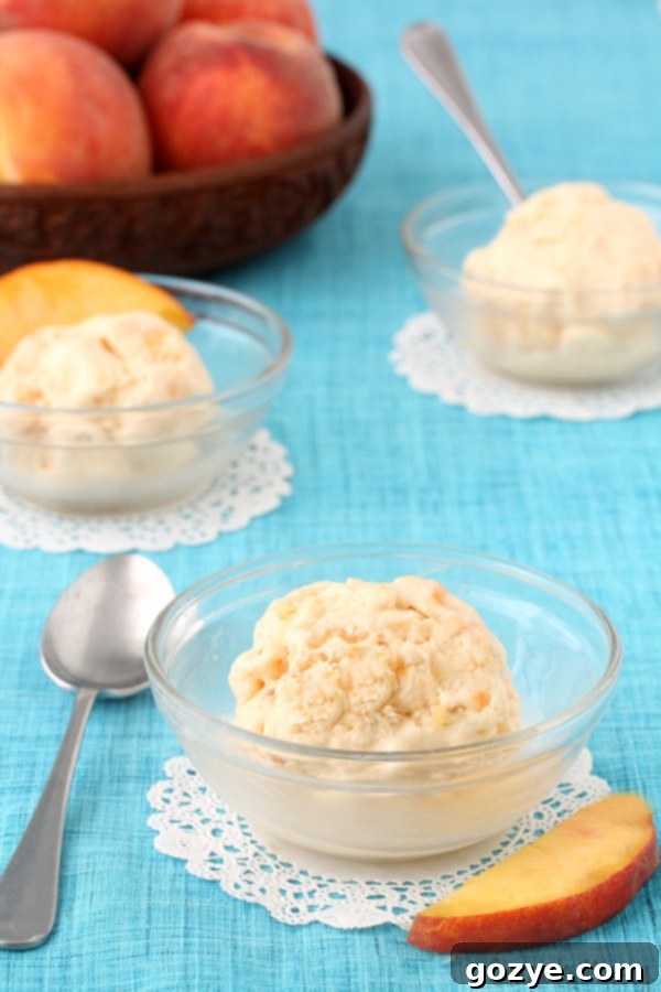 A generous scoop of peaches and cream ice cream in a clear glass bowl with a spoon resting beside it, ready to be enjoyed.