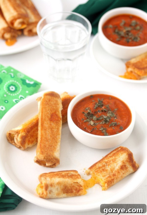 Cozy Grilled Cheese Roll-Ups with Tomato Soup Dip 2 Deliciously golden Grilled Cheese Roll Ups with a side of vibrant Tomato Soup Dipping Sauce, ready to be enjoyed.