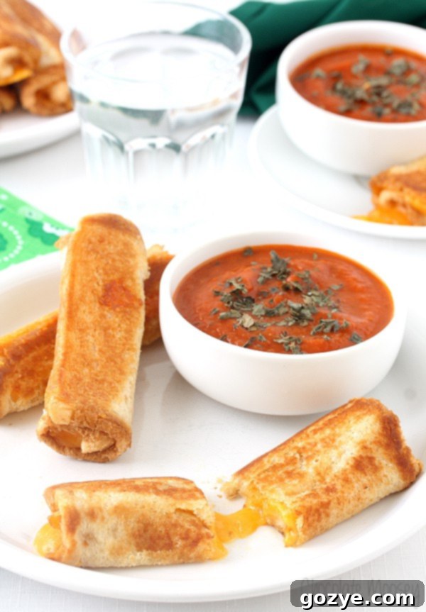Cozy Grilled Cheese Roll-Ups with Tomato Soup Dip 5 A plate piled high with golden Grilled Cheese Roll Ups, ready to be served, with a bowl of tomato soup dipping sauce in the background.