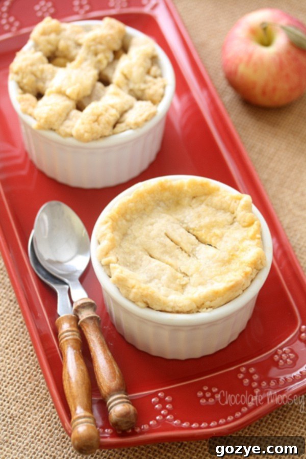 Two mini apple pies in ramekins on a red plate, ready to be served