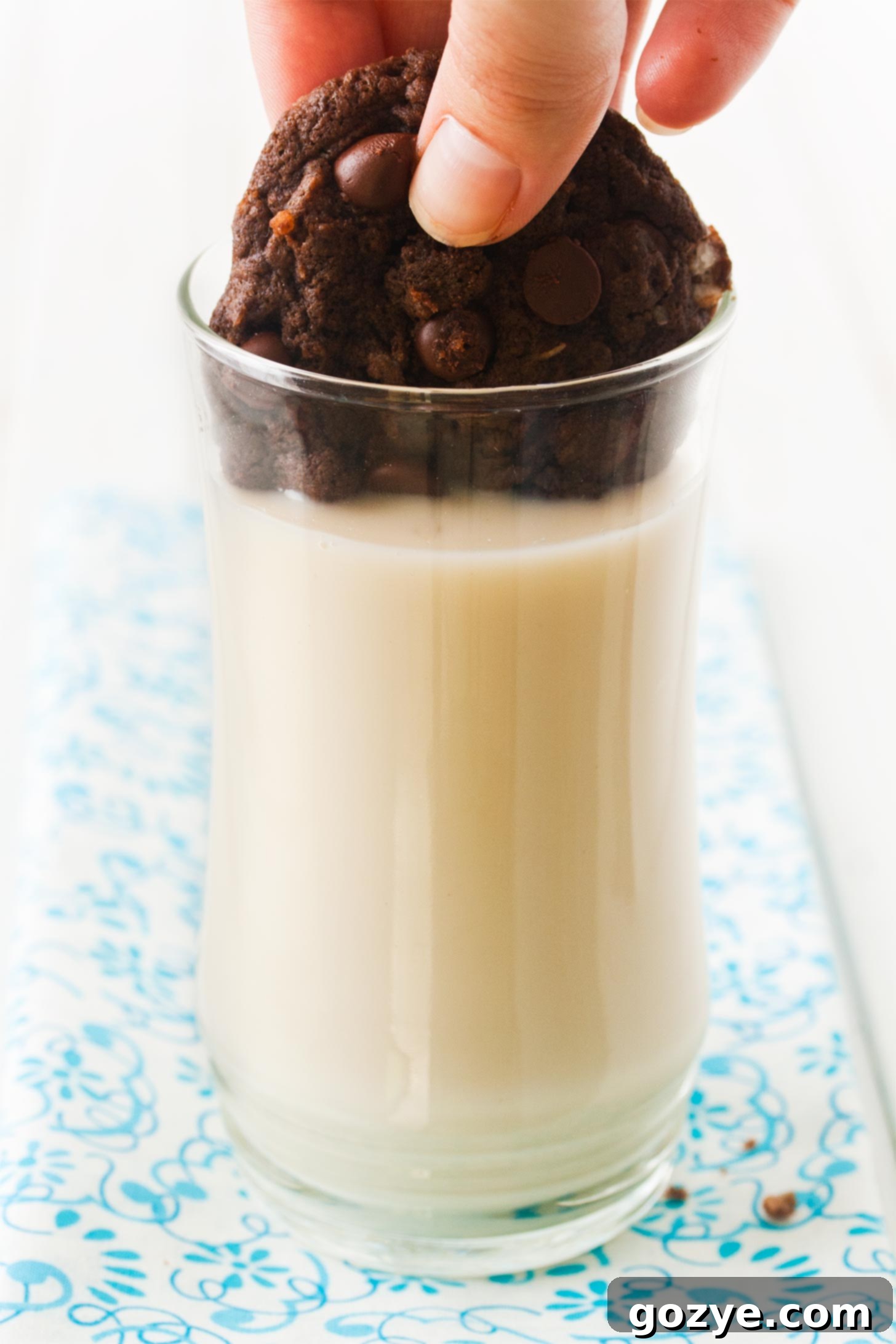 Hand dipping a freshly baked small batch chocolate coconut cookie into a glass of milk