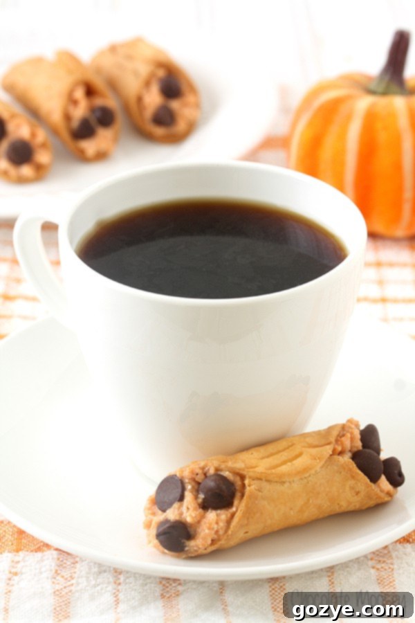 Three Mini Pumpkin Cannolis decorated with chocolate chips, sitting on a rustic wooden board