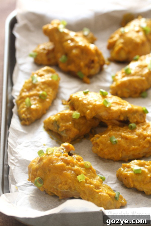 Baking tray lined with parchment paper with curry chicken wings on top, golden brown and glistening with sauce