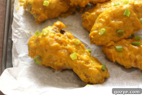 Close up of a single golden brown curry chicken wing resting on parchment paper on a cookie tray, showing crispy skin