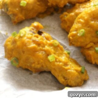 Close up of a golden brown curry chicken wing resting on parchment paper on a cookie tray, with crispy skin and sauce