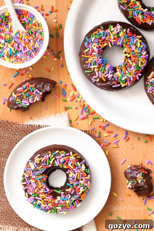 Close-up of three Triple Chocolate Baked Doughnuts with rainbow sprinkles, emphasizing their freshness and rich glaze