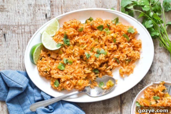 White platter of Spanish rice with a serving spoon and a small individual plate beside it.