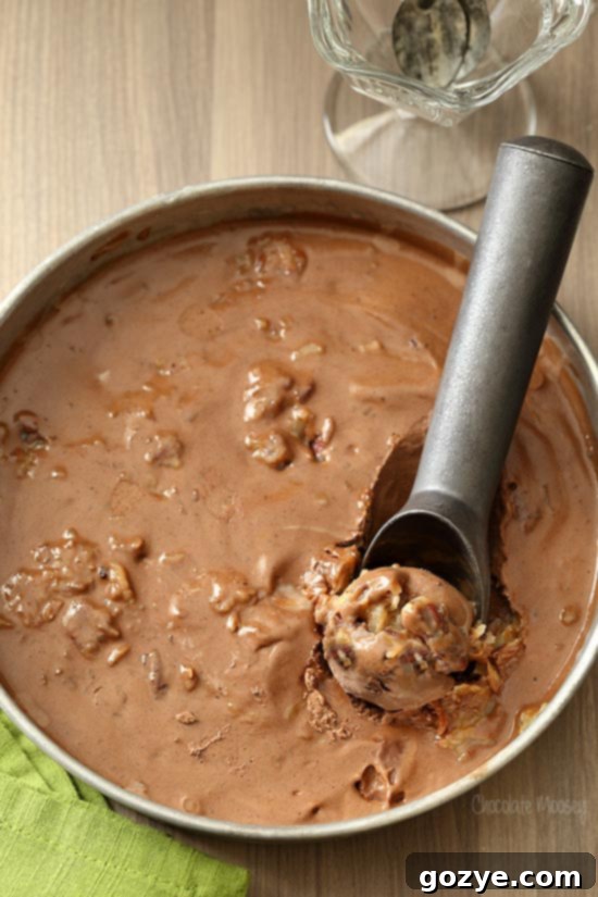 Scooping rich German chocolate ice cream from a round container with a shiny ice cream scooper