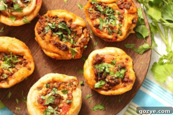 Close-up of the Taco Pizza Roll Ups preparation showing seasoned ground beef and salsa mixture spread on pizza dough, topped with cheese and fresh cilantro, ready to be rolled into individual portions.