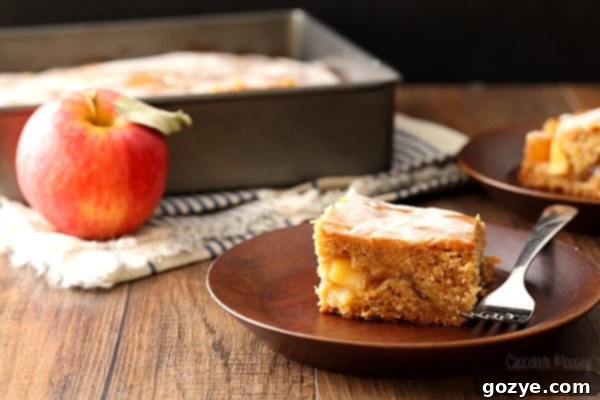 A close-up view of a perfect slice of Apple Fritter Cake, showcasing its fluffy texture, generous apple chunks, and the thick, glistening glaze on top.