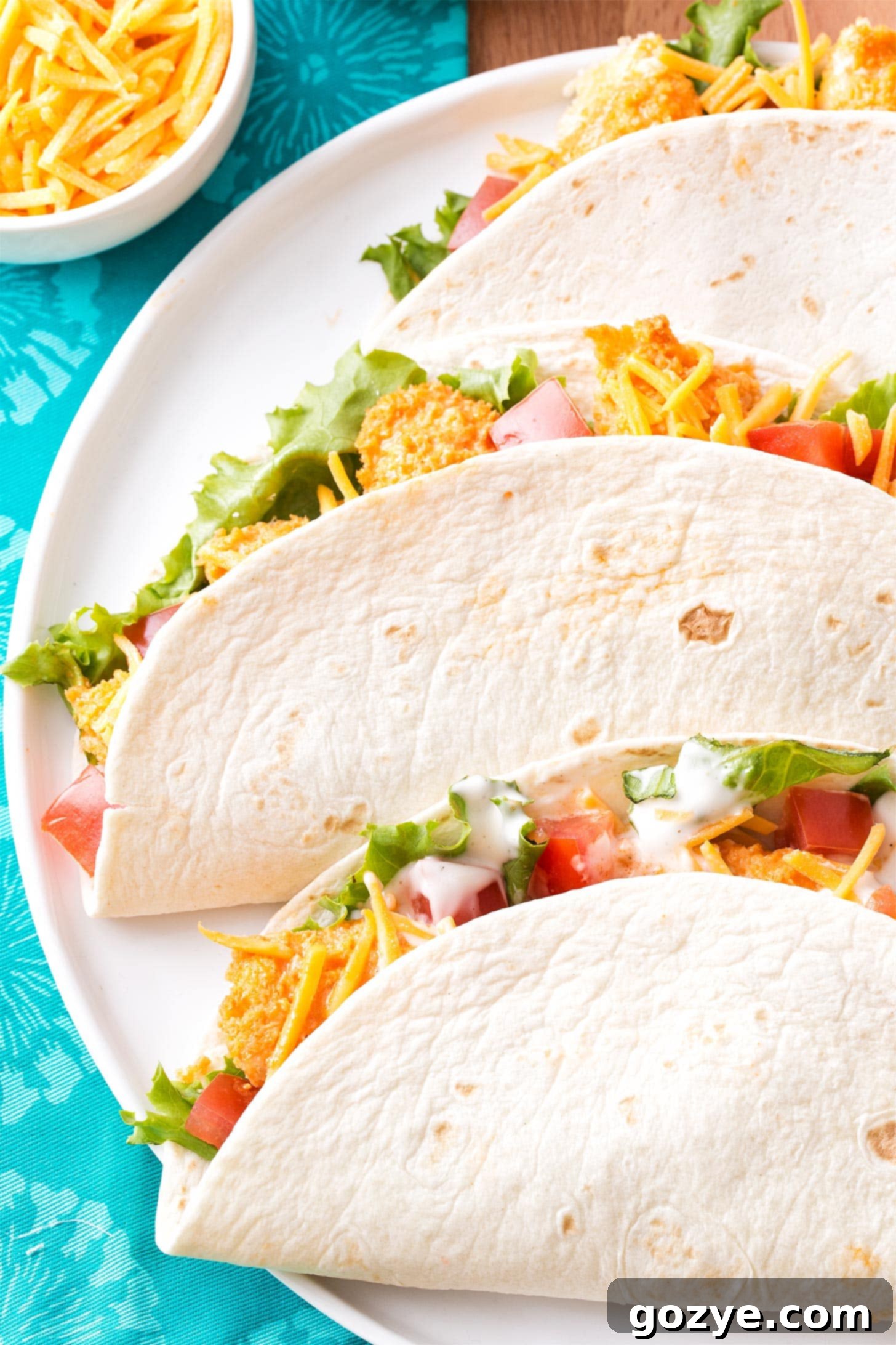 Three Buffalo Chicken Tacos folded on a white plate, showcasing crispy chicken and fresh toppings
