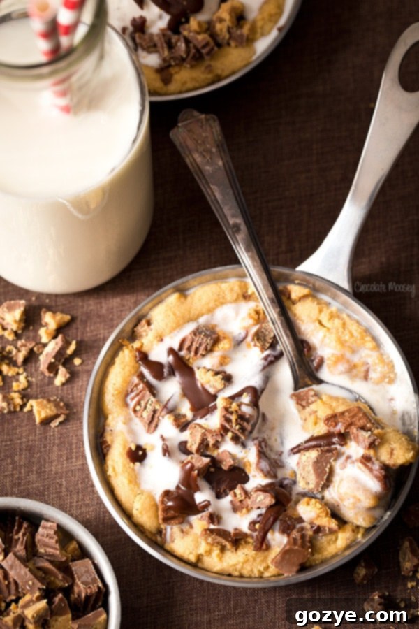 Close-up of a warm Peanut Butter Mini Skillet Cookie with melted chocolate and peanut butter cups, ready for ice cream.