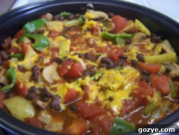 A bowl of vibrant Vegetarian Black Bean Chili garnished with shredded cheddar cheese, with a spoon digging in.