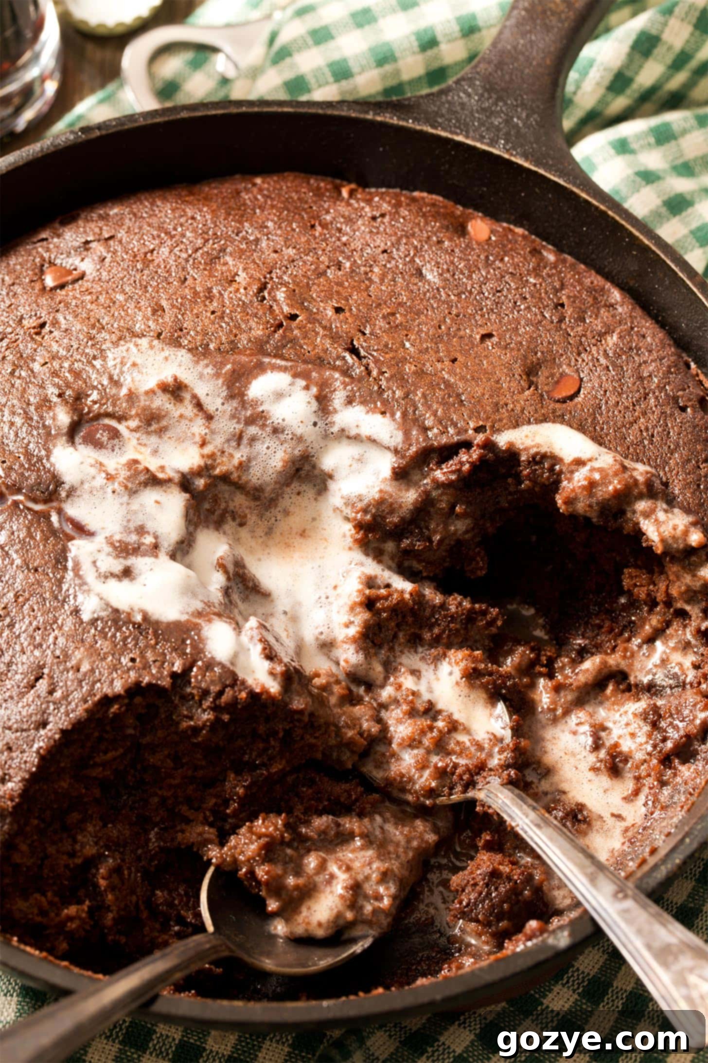 Close up of spoons digging into chocolate skillet cake, highlighting its rich texture