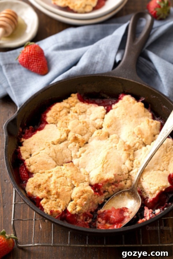 Homemade Strawberry Cobbler in cast iron skillet with golden honey biscuits