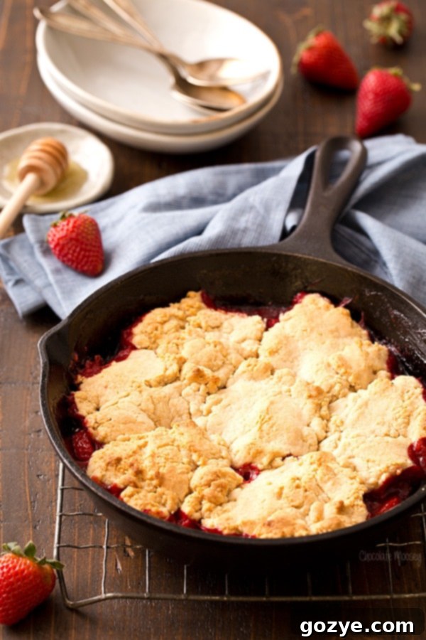 Strawberry shortcake cobbler baking in a cast iron skillet with biscuit topping