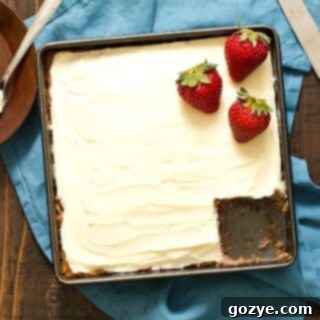 Homemade Strawberry Snack Cake in an 8x8 pan with a piece missing, showing cream cheese frosting