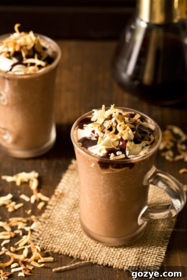 Two glasses of Toasted Coconut Frozen Hot Chocolate garnished with toasted coconut flakes and a drizzle of hot fudge, ready to be enjoyed as a tropical delight.