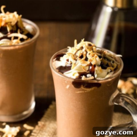 A tall glass of homemade Toasted Coconut Frozen Hot Chocolate, topped with fluffy whipped cream and golden toasted coconut flakes.