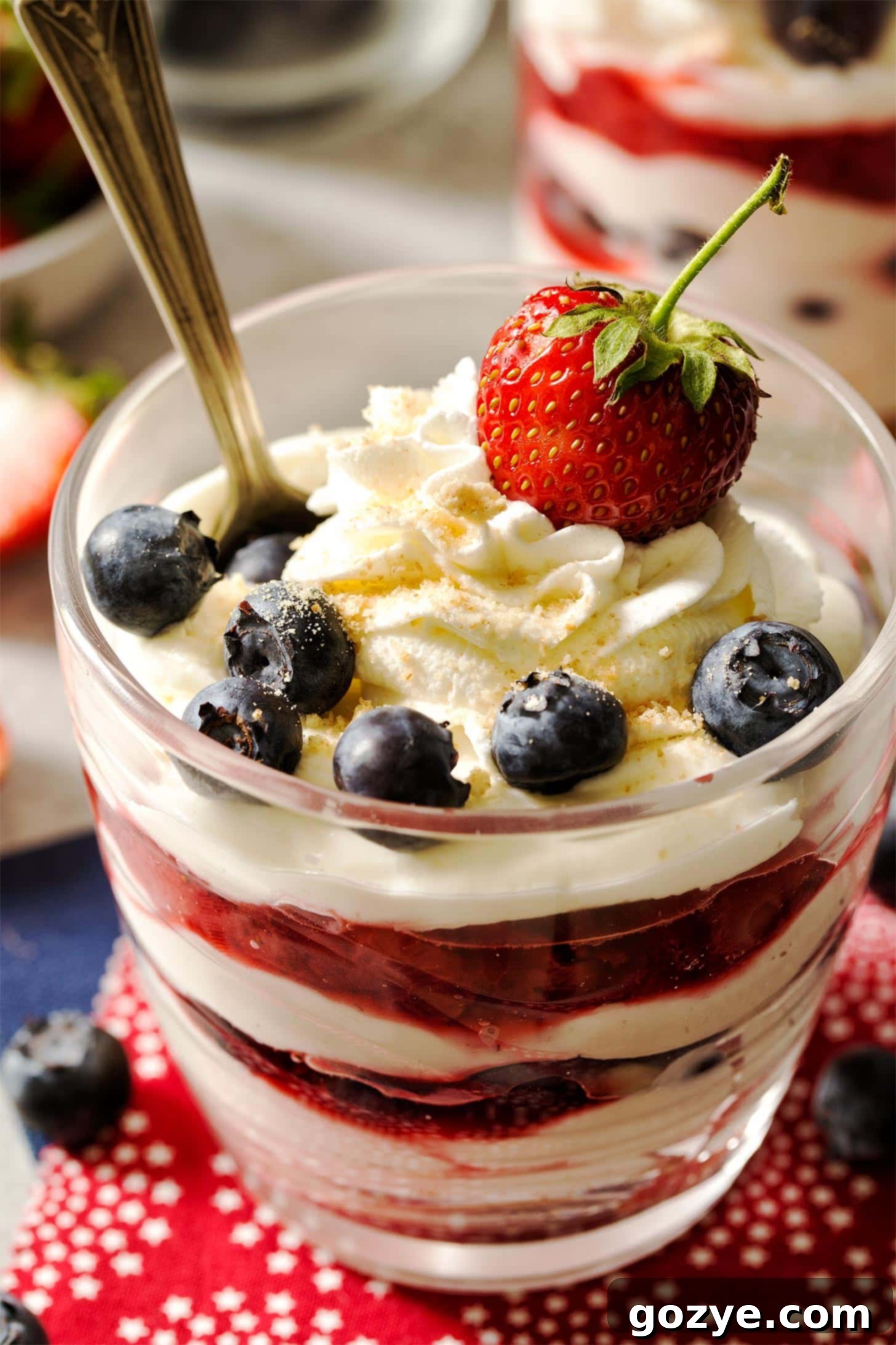 Close-up of two individual No Bake Cheesecake Cups, beautifully layered with creamy filling, crust, strawberries, and blueberries.