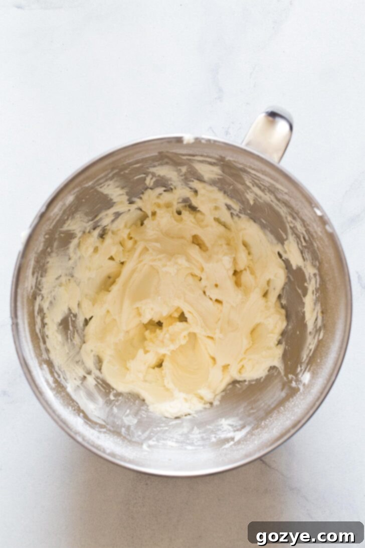 Beating together softened cream cheese, powdered sugar, and vanilla until smooth and creamy for the cheesecake filling base.