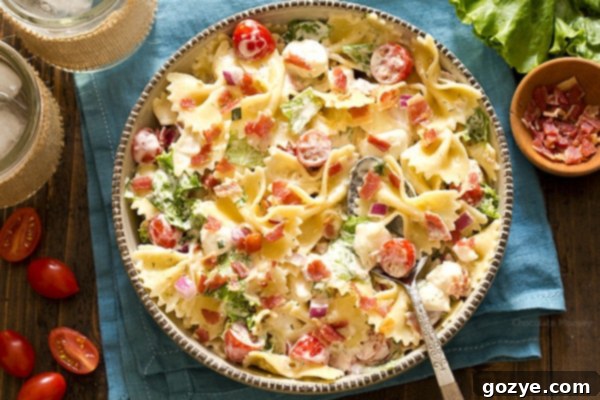A large bowl of vibrant Bacon Ranch Pasta Salad, with a serving spoon nestled in, ready for a gathering