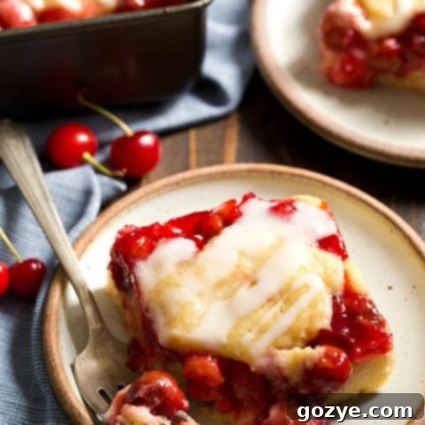 A top-down view of square Cherry Cobbler Bars with a white glaze, some cut and some whole.