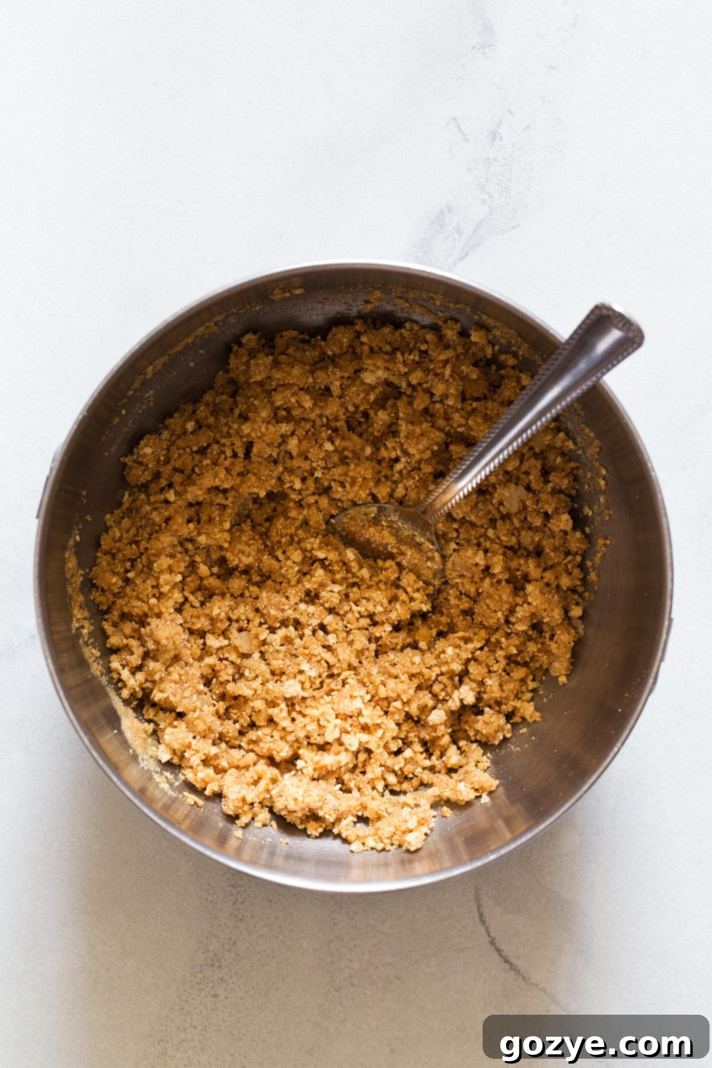 Mixing graham cracker crumbs with butter in a bowl to prepare the cheesecake crust.