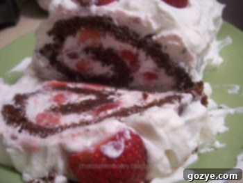 A beautifully prepared California Strawberry Log, a chocolate cake roll filled with strawberries and whipped cream, garnished with more cream on top and fresh berries.