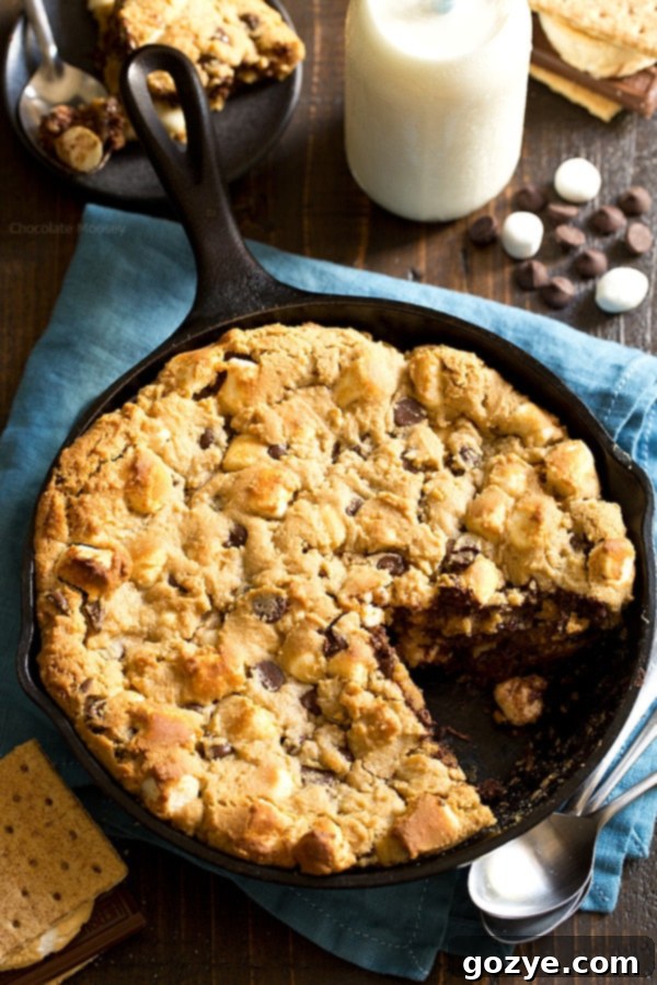 A large serving spoon scooping out a warm, gooey portion of the skillet cookie, showcasing its melted chocolate and marshmallows.