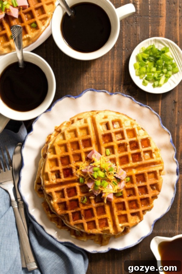 A stack of golden-brown Savory Waffles on a ruffled white plate, garnished with fresh chives