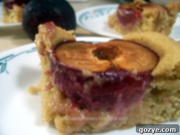 A close-up shot of a sliced Dimply Plum Cake, revealing its moist, tender crumb with perfectly baked, juicy plum pieces and a hint of warm spices.