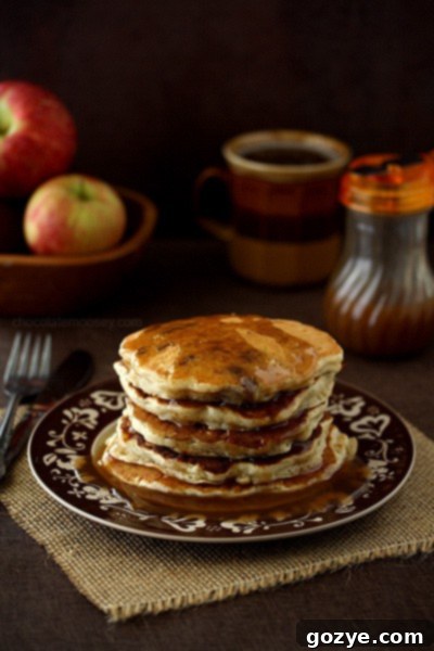Fluffy Apple Sausage Pancakes drizzled with golden Apple Cider Syrup, served with cooked sausage on a plate.