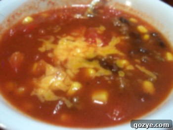A vibrant bowl of homemade taco soup topped with shredded cheddar cheese.