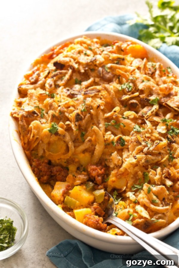 Close-up of golden-brown Cheesy Chorizo Potatoes in a white casserole dish, showing crispy onion topping