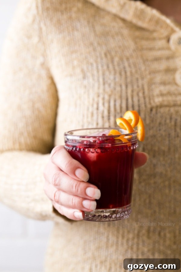 Close-up of a hand holding a glass of Pomegranate Prosecco Punch garnished with an orange slice and pomegranate arils