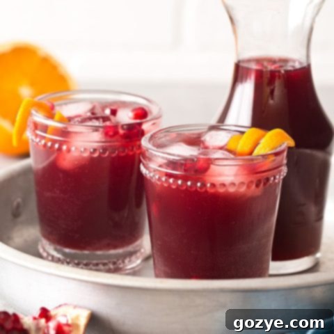 Pomegranate Punch in a pitcher with glasses, ready to be served at a festive event