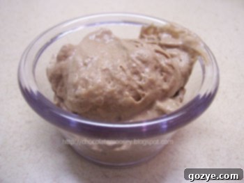 A close-up shot of a creamy, decadent chocolate mousse in a glass serving dish, garnished with a light dusting of cocoa powder or chocolate shavings.