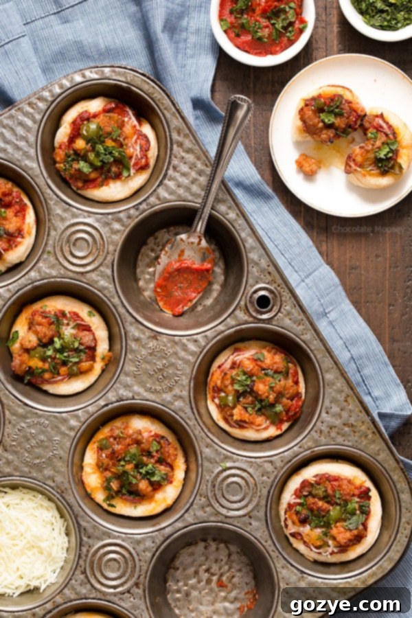 A baking sheet filled with freshly baked Italian Sausage Pizza Bites, each in a muffin cup, with golden crusts and bubbly cheese