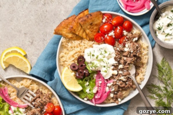Close-up of Slow Cooker Gyro Rice Bowls showcasing shredded lamb, fresh vegetables, feta, and tzatziki sauce.